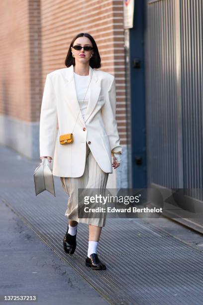 Guest wears sunglasses, gold earrings, a white t-shirt, a white oversized blazer jacket, an orange matte leather embossed FF monogram pattern micro...