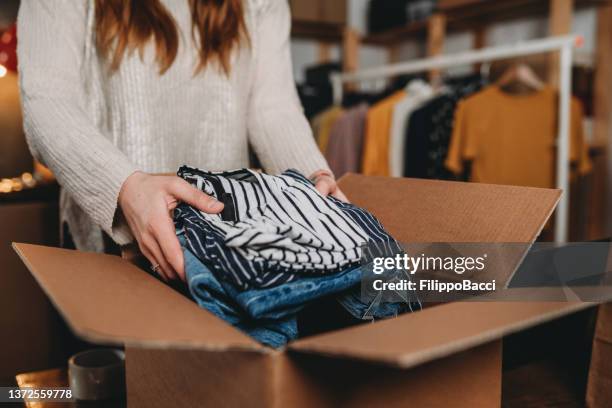 eine millennial-frau bereitet den versand einiger kleidungsstücke in ihrem neuen online-shop vor - clothing stock-fotos und bilder