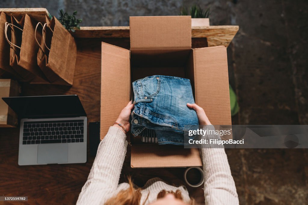 A millennial woman is preparing the shipment of some clothes in her new online shop