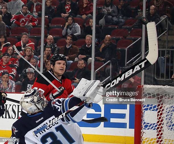 Ondrej Pavelec of the Winnipeg Jets deflects a shot of the tip of his stick as David Clarkson of the New Jersey Devils looks for a rebound at the...