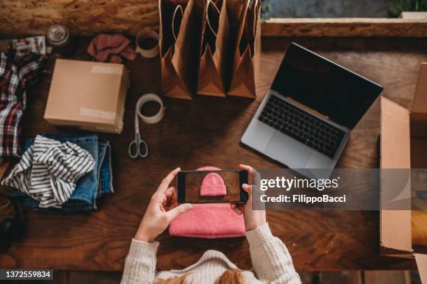 a woman is photographing a pink hat to post a new item on her online shop - white hat fashion item stockfoto's en -beelden