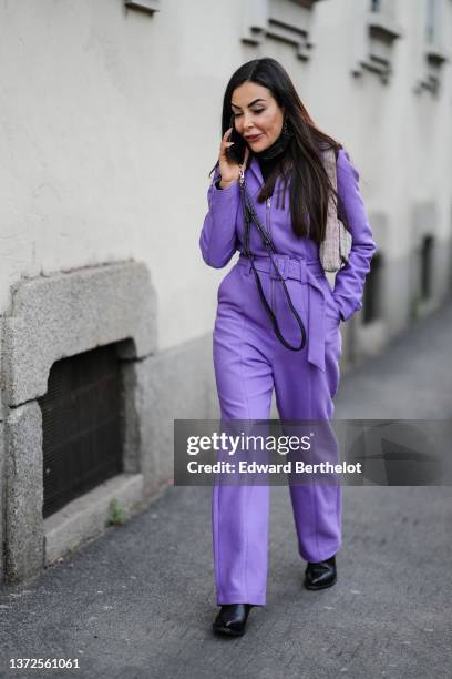 Guest wears a purple zipper / belted jumpsuit, a rhinestones shoulder bag, a black turtleneck pullover, black shiny leather pointed block heels ankle...