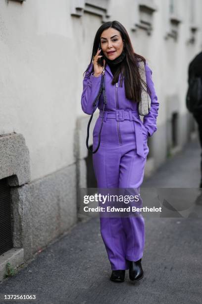 Guest wears a purple zipper / belted jumpsuit, a rhinestones shoulder bag, a black turtleneck pullover, black shiny leather pointed block heels ankle...