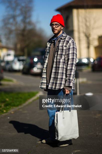 Guest wears a red wool beanie, black glasses, a navy blue and white print pattern scarf, a brown sweater, a beige and black checkered print pattern...