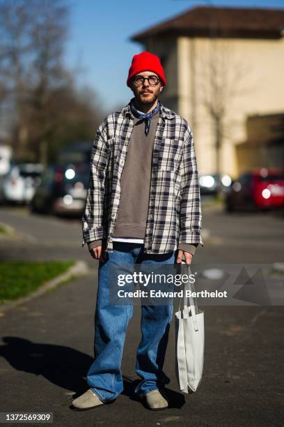 Guest wears a red wool beanie, black glasses, a navy blue and white print pattern scarf, a brown sweater, a beige and black checkered print pattern...