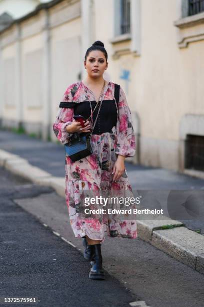 Guest wears diamond earrings, a pale pink and green flower print pattern long sleeves / ruffled midi dress, a black square tank-top buttoned corset,...