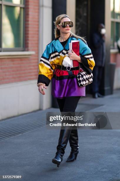 Guest wears brown ski sunglasses, a black t-shirt, a blue / beige / black / gold / red / purple shiny silk pattern belted jacket, a black and white...