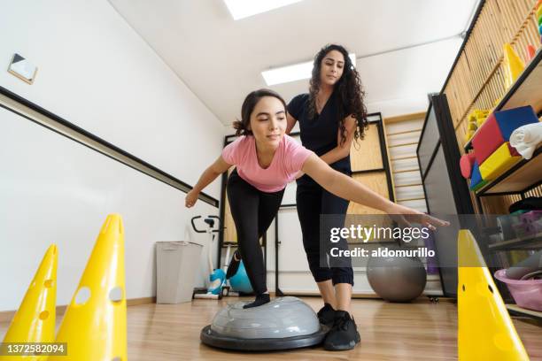 young woman standing on balance ball and stretching in physical therapy - fitness ball stock pictures, royalty-free photos & images