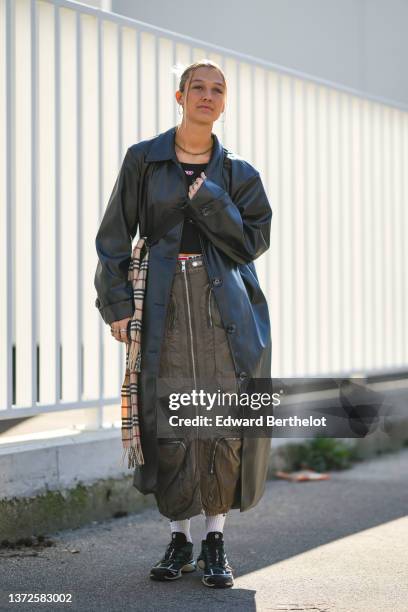 Guest wears gold earrings, a gold necklace, a black shiny leather long coat, a black cropped t-shirt from Diesel, gold rings, a beige with black and...