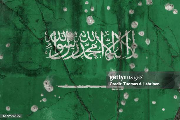 full frame photo of a weathered flag of saudi arabia painted on a cracked wall with bullet holes. - saudi arabian flag stockfoto's en -beelden