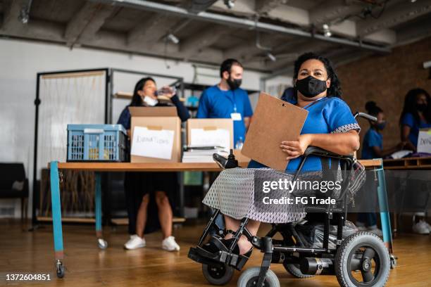 portrait of a disabled mature woman working in a community charity donation centre - wearing protective face mask - community health centre stock pictures, royalty-free photos & images