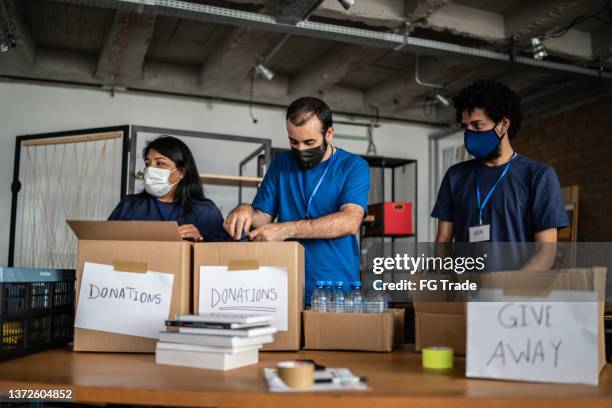 group of volunteers working in community charity donation centre - using protective face mask - giving tuesday stock pictures, royalty-free photos & images