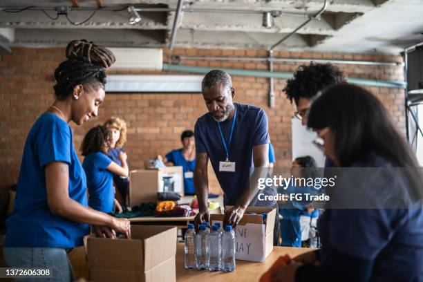 volunteers arranging donations in a community charity donation center - ajuda humanitária imagens e fotografias de stock