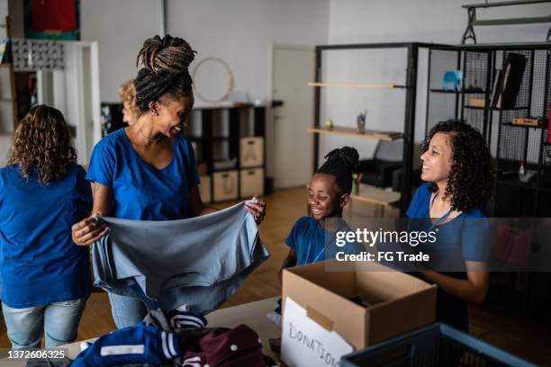 des bénévoles organisent des dons de vêtements dans un centre de dons caritatif communautaire - charity benefit photos et images de collection