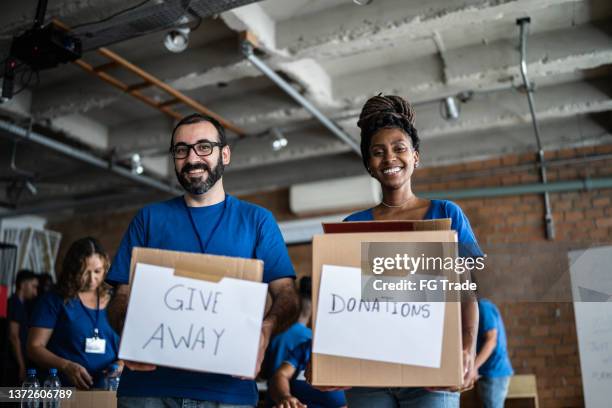 portrait of volunteers holding charity boxes in a community center - selfless stockfoto's en -beelden