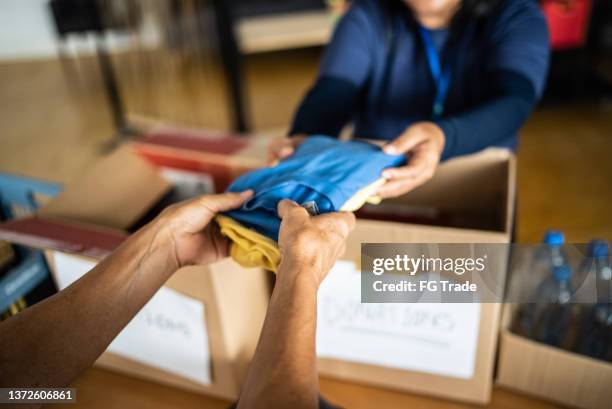 volunteer's hand giving donations to a person at a community center - liefdadigheidsinstelling stockfoto's en -beelden