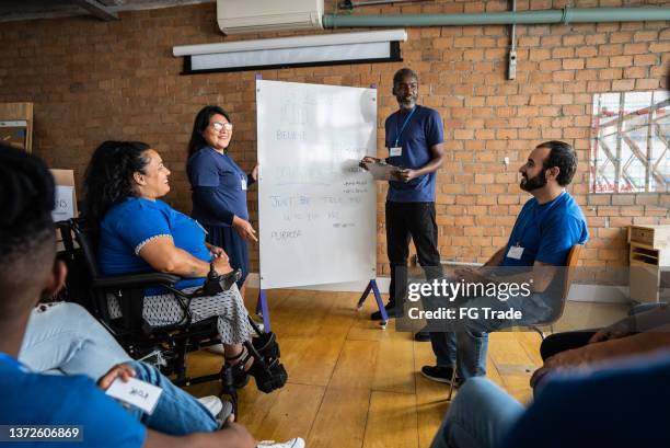 mature man talking in a meeting at a community center - including a disabled person - showing empathy at work stock pictures, royalty-free photos & images