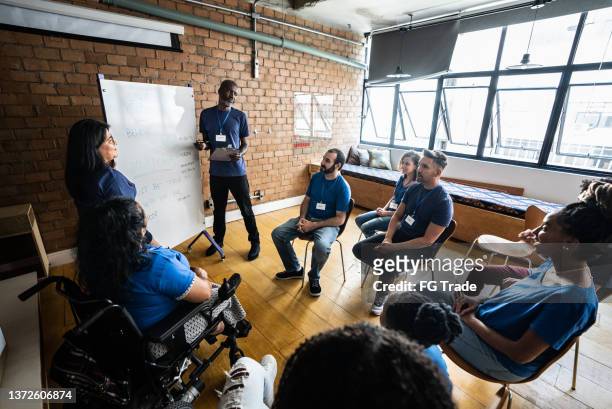 mature man talking in a meeting at a community center - including a disabled person - benefietactie stockfoto's en -beelden