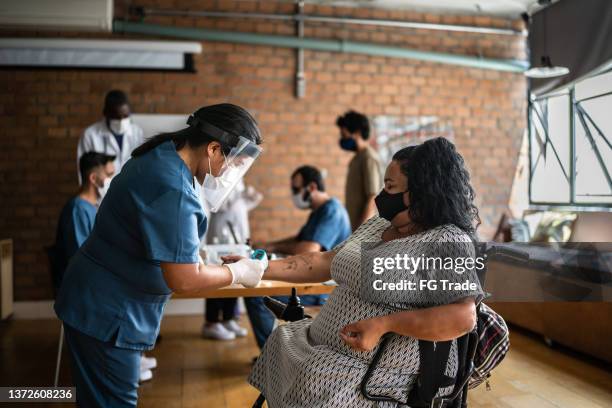 nurse taking the temperature of a mature woman in a medical clinic - including a disabled person - covid persons with disabilities stock pictures, royalty-free photos & images