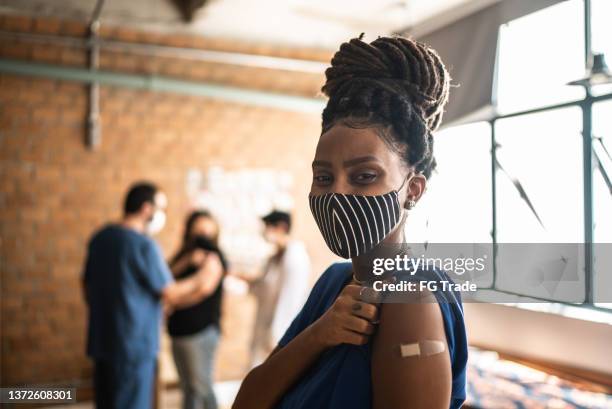 porträt einer jungen frau, die nach der impfung ihren arm zeigt - mit gesichtsmaske - vaccination center stock-fotos und bilder