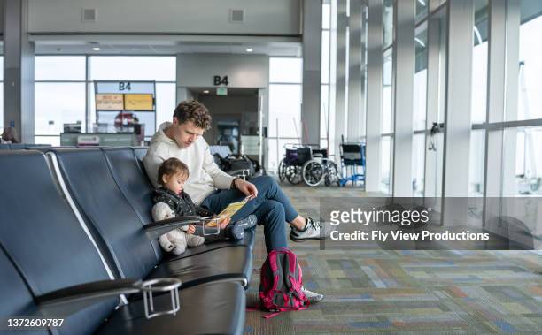 dad reading book to toddler while waiting for flight at the airport - baby on the move stock pictures, royalty-free photos & images