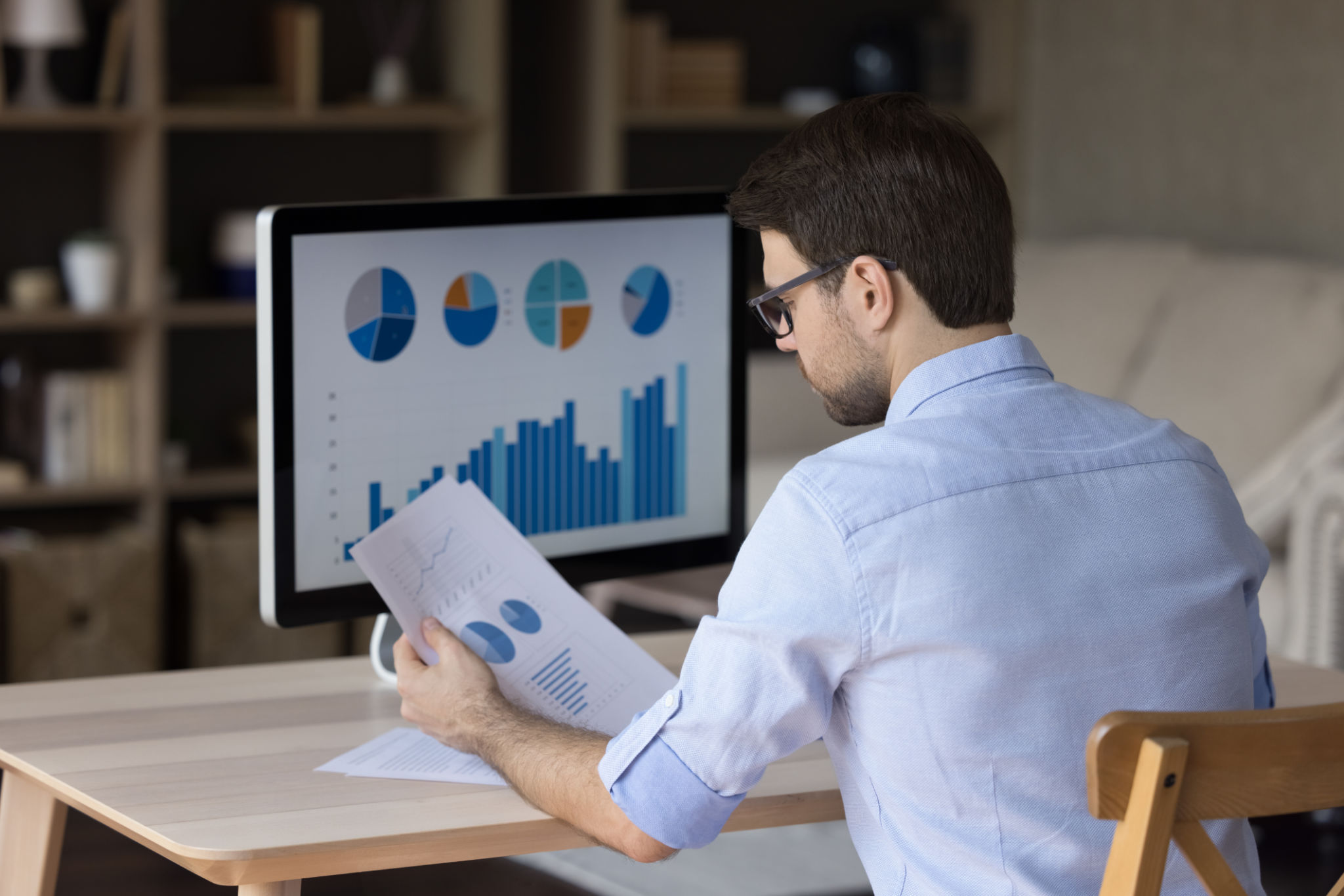 Focused millennial business man analyzing marketing reports on desktop monitor Focused millennial business man analyzing marketing reports on desktop monitor