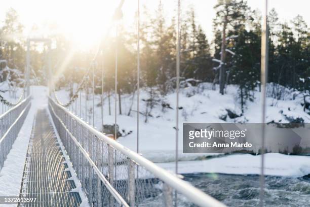 suspension bridge over the juutuanjoki river in winter lit by the sun. - inari finland bildbanksfoton och bilder