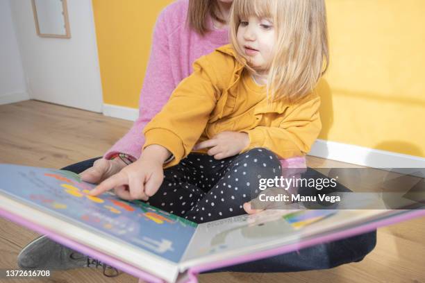 little girl sitting on her mother's lap as she excitedly shows her the pictures in a book. - girl pointing bildbanksfoton och bilder