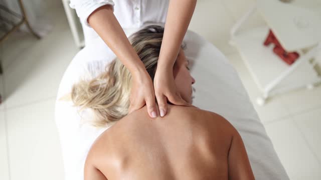 Massage therapist working on a female client's back in a spa