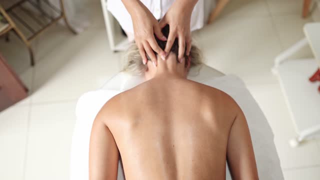 Therapist massaging the back of a female client lying on a table