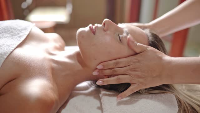Therapist massaging the face of a female client at a health spa