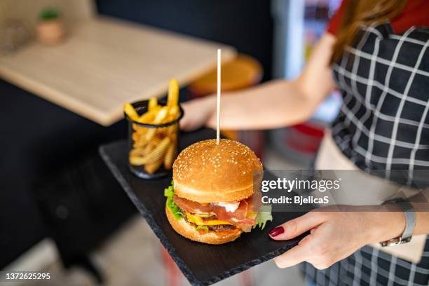 waitress carrying a hamburger with french fries in fast food restaurant - burger and fries stockfoto's en -beelden