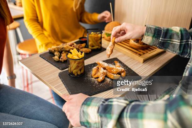 group of friends enjoying eating fried chicken fingers, burger and french fries - chicken fingers stockfoto's en -beelden