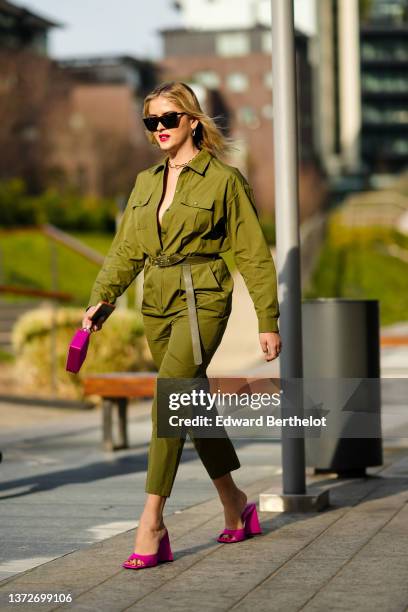 Valentina Ferragni wears black sunglasses, gold earrings, a gold large chain necklace, a khaki shirt jumpsuit, a khaki shiny leather belt, a pink...