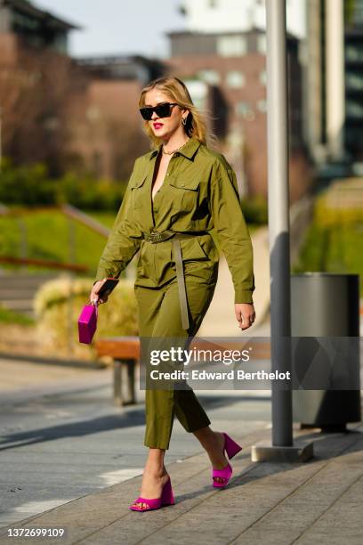 Valentina Ferragni wears black sunglasses, gold earrings, a gold large chain necklace, a khaki shirt jumpsuit, a khaki shiny leather belt, a pink...