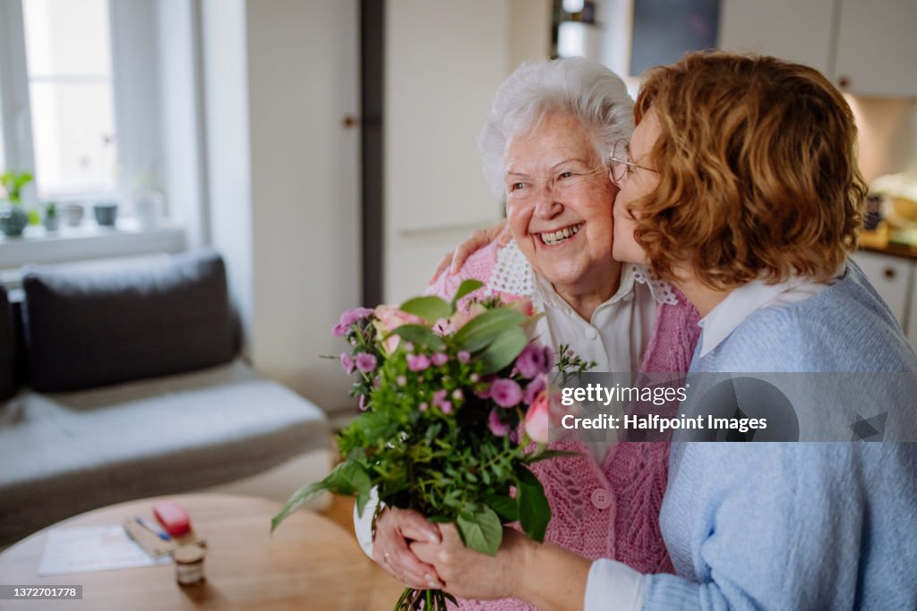 Happy senior mother getting flowers from her adult daughter at home, mother's day concept.