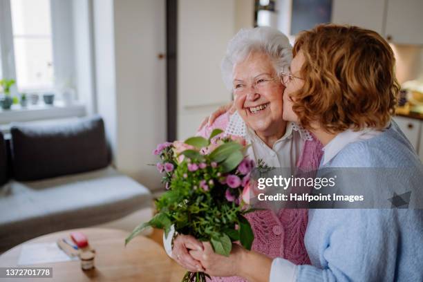 happy senior mother getting flowers from her adult daughter at home, mother's day concept. - fête des mères photos et images de collection