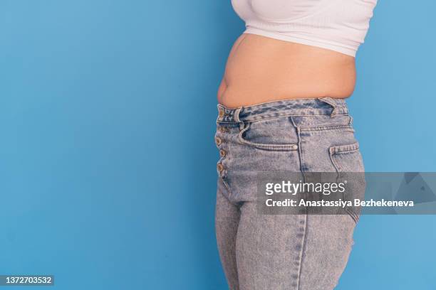 overweight girl in gray jeans against a blue background - abdômen humano - fotografias e filmes do acervo