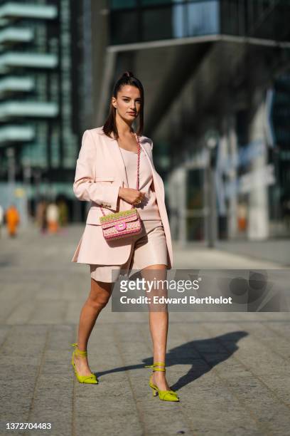 Gabrielle Caunesil wears a pale pink V-neck t-shirt, a pale pink blazer jacket, beige shiny leather shorts, a green / pink / yellow braided tweed...