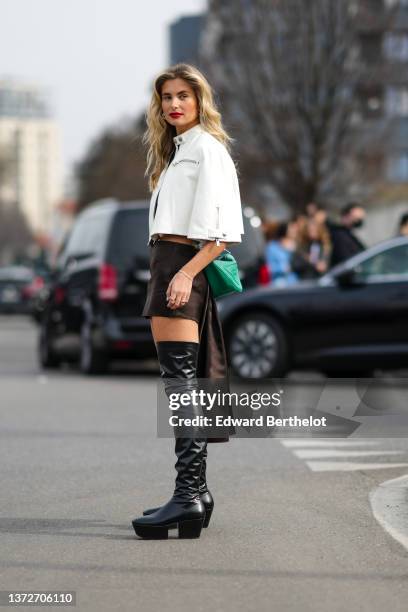 Xenia Adonts wears a white leather cropped cloak jacket, a dark brown satin tube short skirt with a long back-train, a green shiny leather with large...