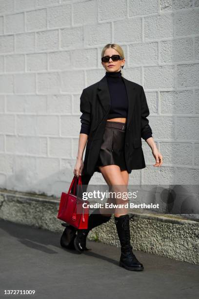 Caroline Daur wears black sunglasses from Prada, a black cropped turtleneck pullover, a silver and black earring from Prada, a black oversized blazer...