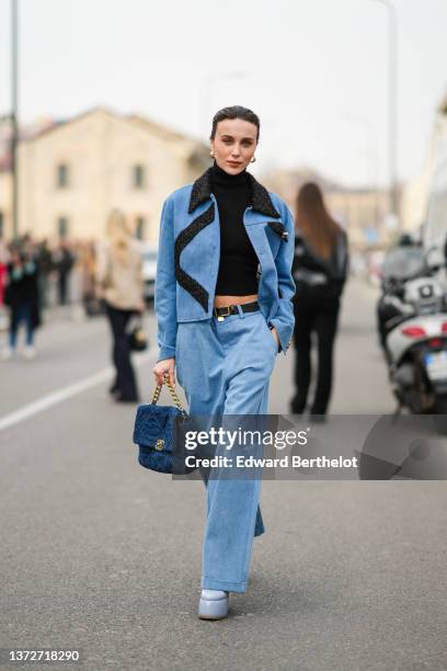 Mary Leest wears gold earrings, a black turtleneck pullover, a blue denim with embroidered black fringed pattern jacket, matching blue denim large...