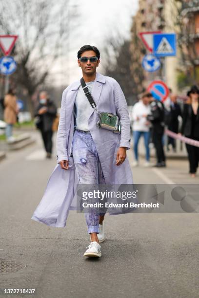 Rahi Chadda wears gray sunglasses, a pale gray t-shirt, a pale purple long oversized coat, pale purple print pattern / tie and dye print pattern...