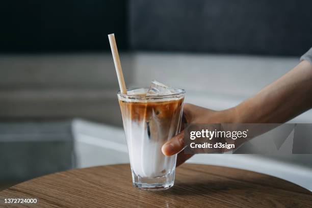 cropped shot of woman's hand holding a glass of iced coffee with eco friendly straw served on the wooden table in coffee shop - rietje stockfoto's en -beelden