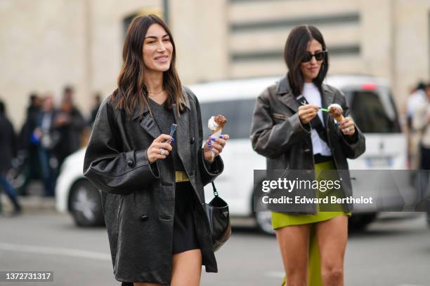 Gilda Ambrosio wears black sunglasses from Ray Ban, a white t-shirt, a black shiny leather crossbody bag from Prada, a black faded leather oversized...