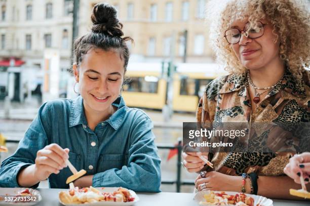 zwei teenager-mädchen essen currywurst mit pommes frites in berlin - berlin prenzlauer berg stock-fotos und bilder