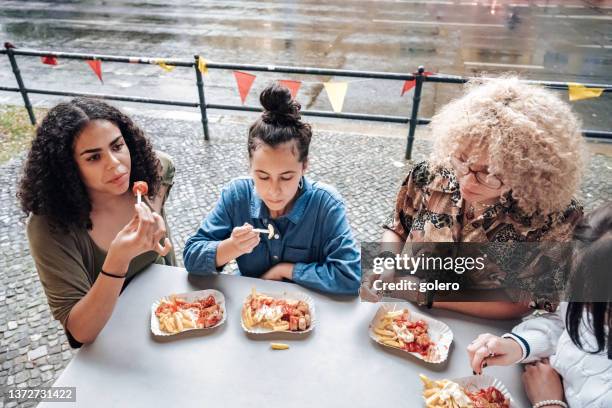 four teenage girls eating curry sausage with french fries in berlin - currywurst stock pictures, royalty-free photos & images