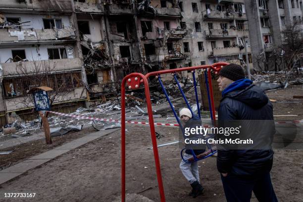 Boy plays on a swing in front of a damaged residential block hit by an early morning missile strike on February 25, 2022 in Kyiv, Ukraine. Yesterday,...