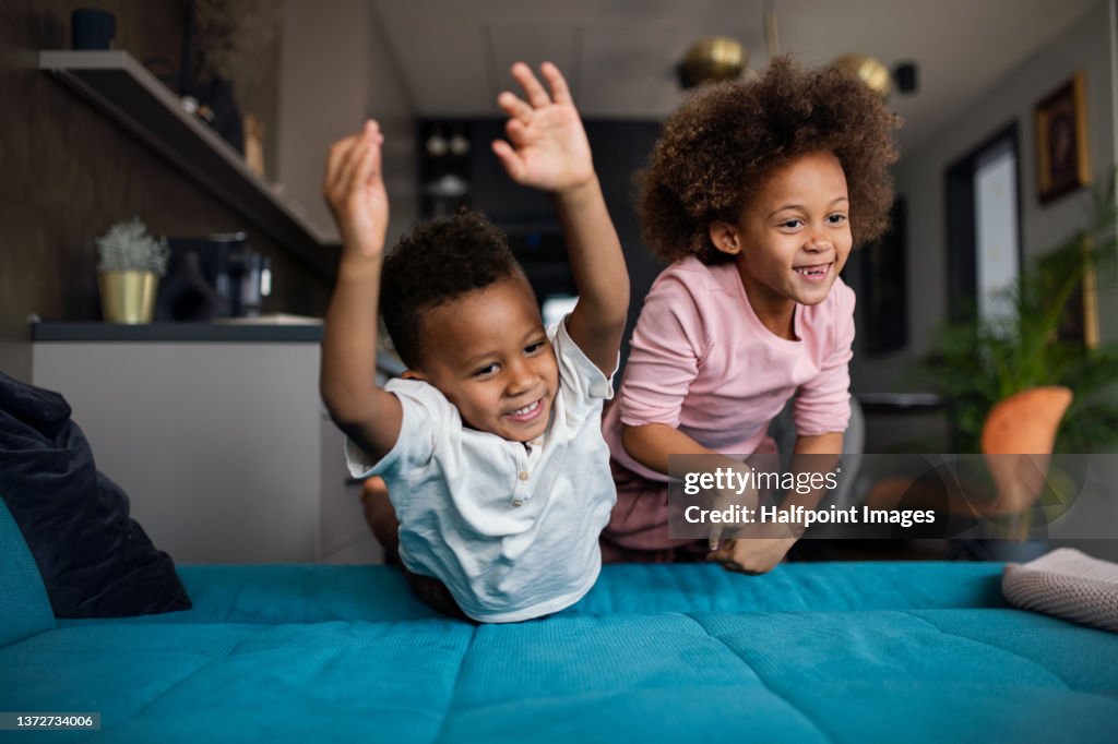 Two happy multiracial children jumping on sofa at home.
