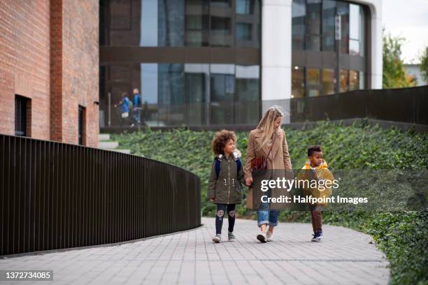 happy mother taking children home from school, walking outdoors in street, multiracial family. - au pair fotografías e imágenes de stock